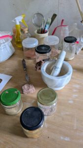 Farben herstellen mit Pigmenten verschiedene Einmachgläser, die mit erde gefüllt sind und ein mörser aus marmor stehen auf dem tisch