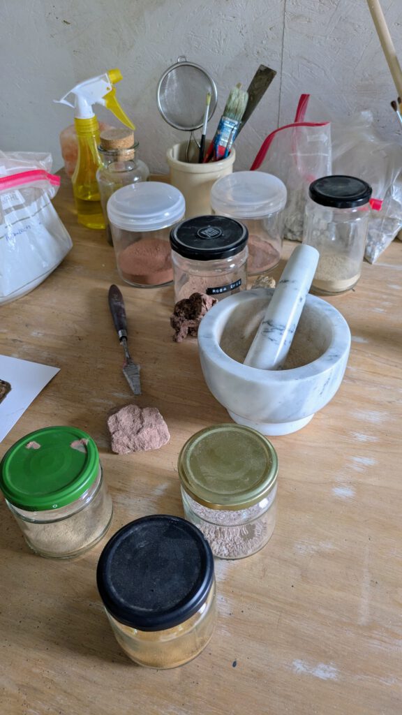 Farben herstellen mit Pigmenten verschiedene Einmachgläser, die mit erde gefüllt sind und ein mörser aus marmor stehen auf dem tisch